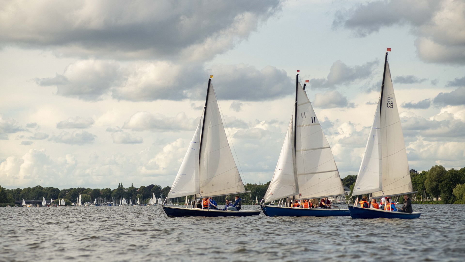 Drei Segelboote auf der Alster in Hamburg mit wolkigem Himmel